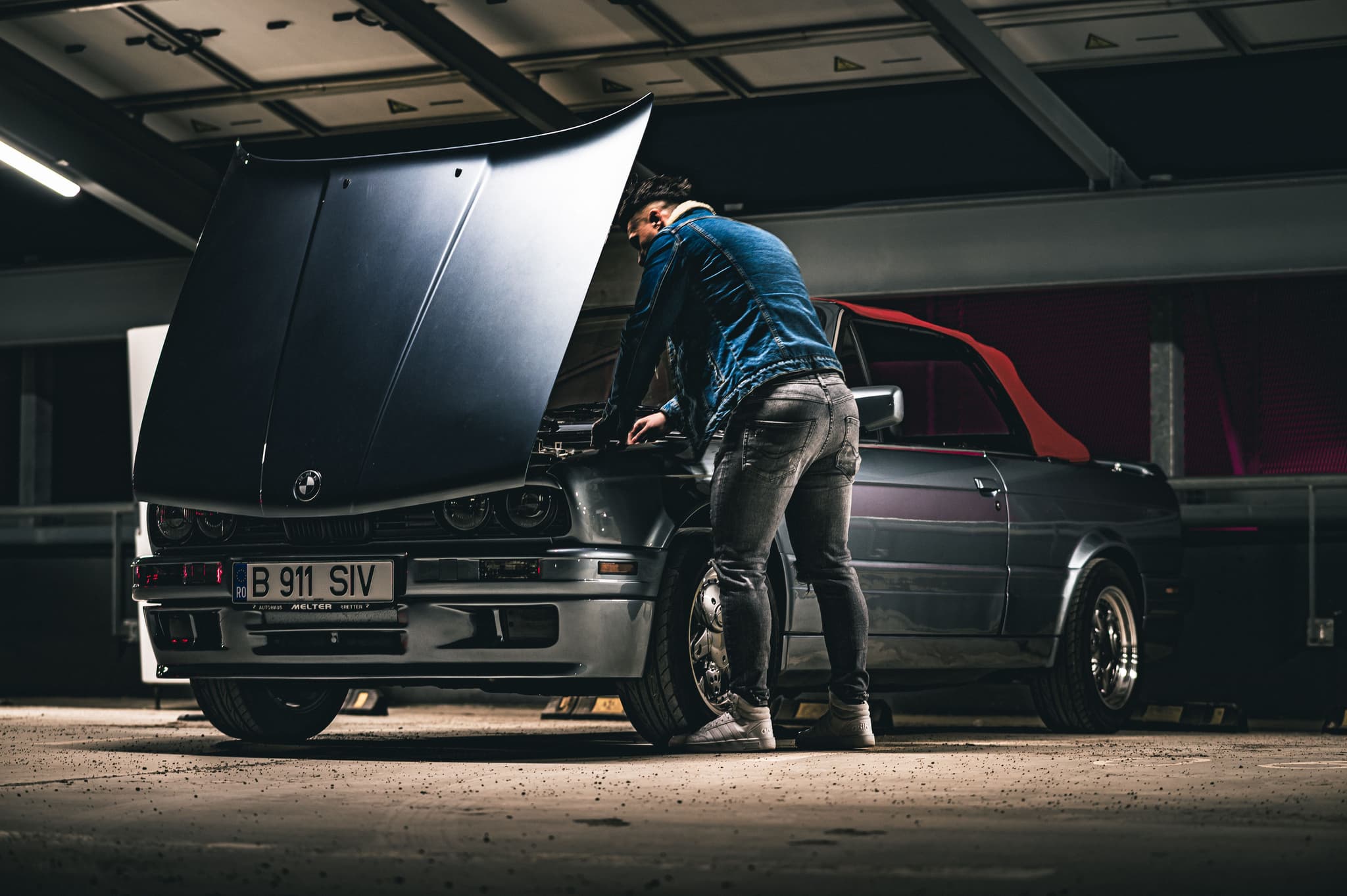 A man works on the engine of a classic convertible car in a garage, highlighting automotive repair.